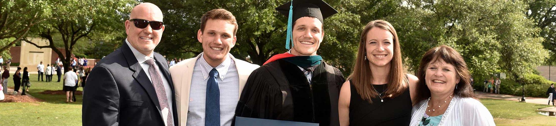 研究生 in cap and gown with family outside